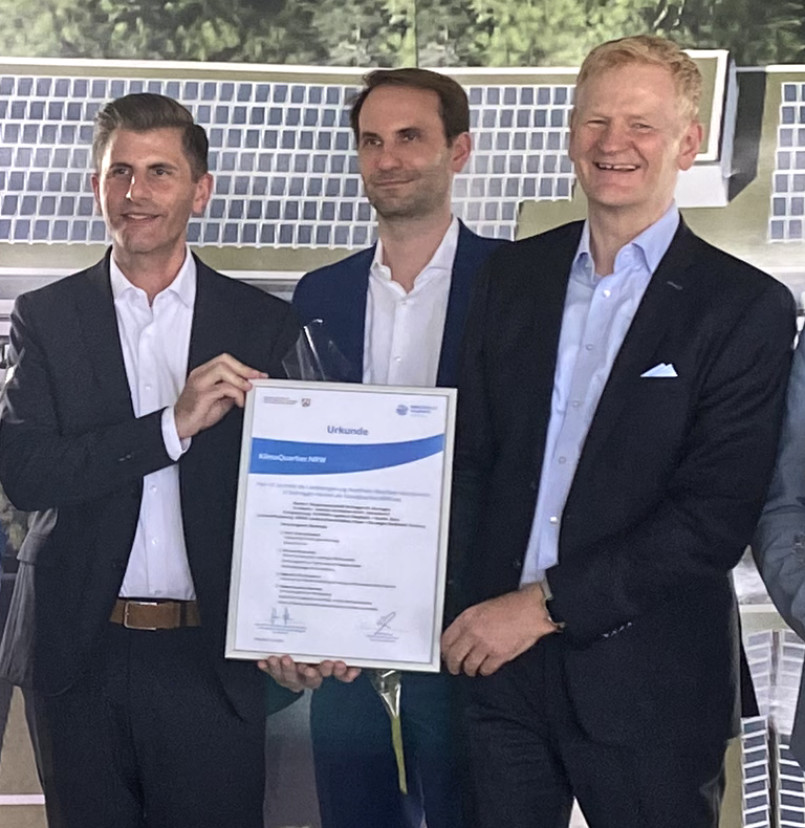 Christian van Kan, Dipl.-Ing. Michael Müller und Martin Klemmer halten die Urkunde zum KlimaQuartier.NRW in die Kamera.